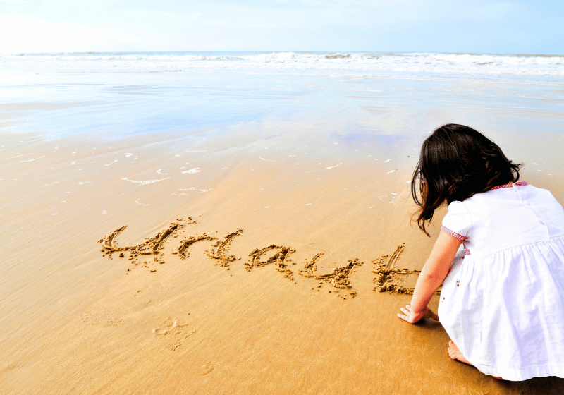 Kind am Strand schreibt das Wort Urlaub in den Sand